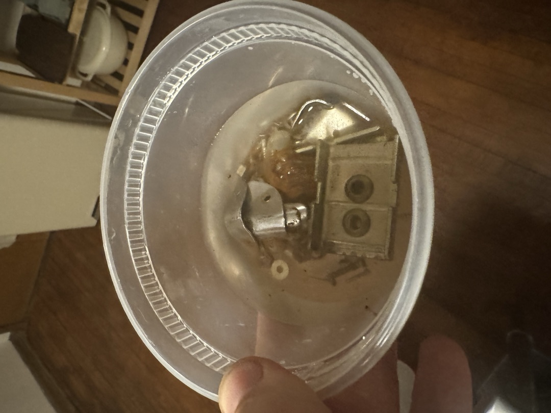 A small metal part soaking in solvent, being cleaned up