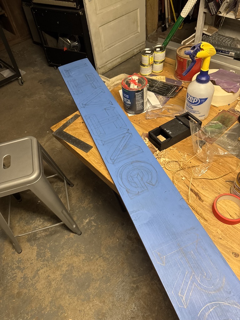 The blue board with the lettering laid out in pencil, each letter drawn as a dimensional block