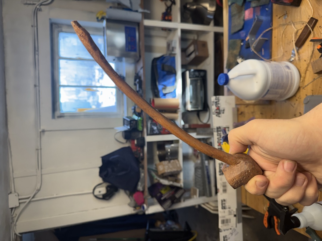 The finished pipe, darkened, held against the workshop